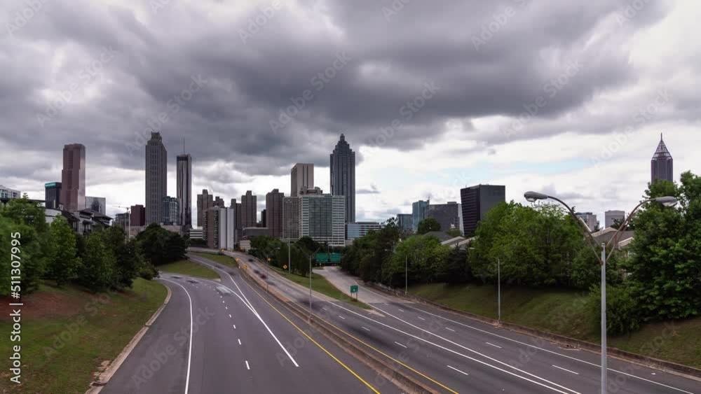 Panning down time lapse of downtown Atlanta from Jackson Street bridge overlooking the highway with motion blur on the vehicular traffic traveling on the roadway below and heavy cloud cover above. Panning down time lapse of downtown Atlanta from Jackson Street bridge overlooking the highway with motion blur on the vehicular traffic traveling on the roadway below and heavy cloud cover above.