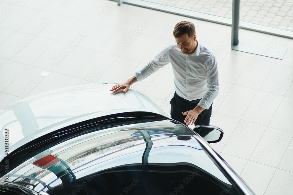 Man adult customer male buyer client chooses auto wants to buy new automobile touch check car in showroom vehicle salon dealership store motor show indoor. Sales concept Man adult customer male buyer client chooses auto wants to buy new automobile touch check car in showroom vehicle salon dealership store motor show indoor. Sales concept