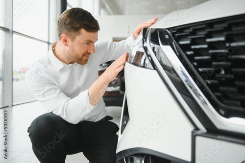 Young handsome man at show room standing near car