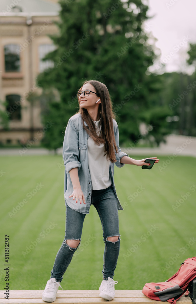 Stylish cheerful young lady dancing on a bench listening to music with earplugs on. Stylish cheerful young lady dancing on a bench listening to music with earplugs on.