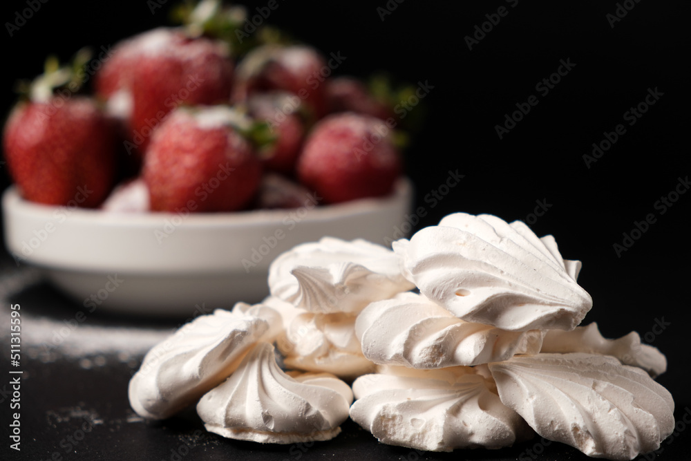 Meringue close up and strawberries in a plate on a black background. Fruit desserts.
