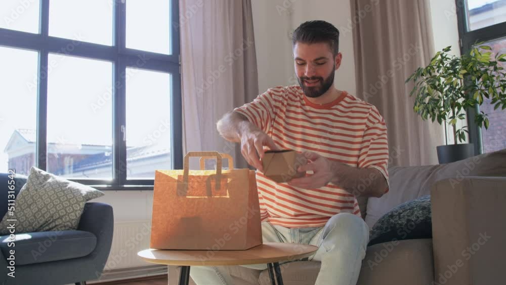 consumption, eating and people concept - smiling man unpacking takeaway food in paper bag at home consumption, eating and people concept - smiling man unpacking takeaway food in paper bag at home