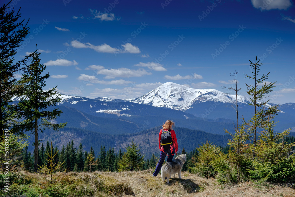 Happy girl resting with her siberian husky dog together outdoor. Snowy mountains in the background. Human and animal friendship concept