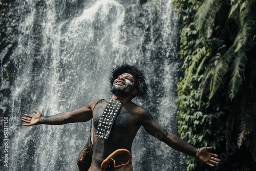Papua man of Dani tribe feel free spread out his hands and breath  against waterfall at greenery forest photo