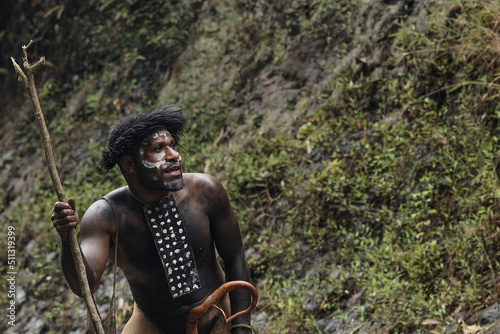 Dani Tribe man from Papua Indonesia wearing traditional costume and koteka is looking around to get the food. 