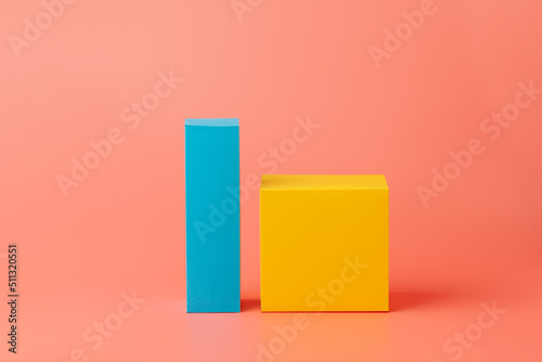 Yellow cube and blue paper rectangle. Geometric shapes made of paper or cardboard isolated on a pink background.