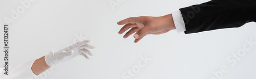 cropped view of groom and bride reaching each other hands isolated on grey, banner.