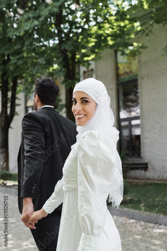 joyful muslim bride in wedding dress holding hands with groom in suit.