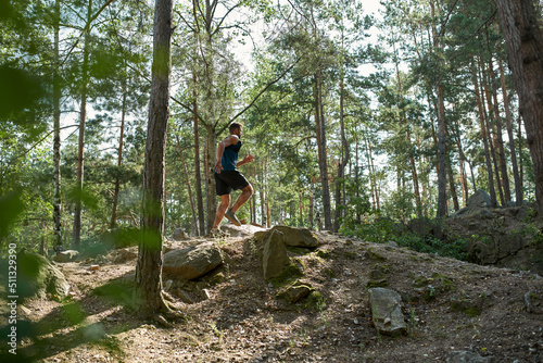 Side view of sportsman running on hill in forest