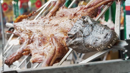 Grilling whole crocodile body in street food at Thailand. Meat exotic is rotating and cooking on fire barbecue in asian street food