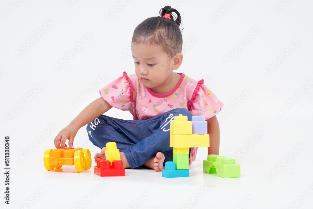 Lovely little cute asian girl playing on the floor with lots of colorful plastic blocks in studio, isolated on white background Lovely little cute asian girl playing on the floor with lots of colorful plastic blocks in studio, isolated on white background