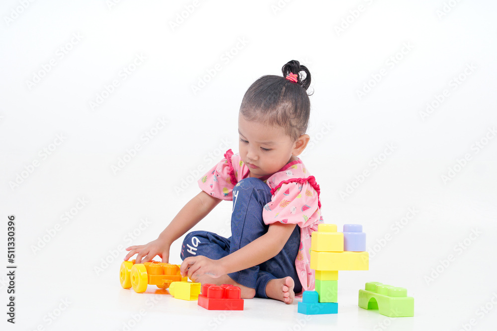 Lovely little cute asian girl playing on the floor with lots of colorful plastic blocks in studio, isolated on white background Lovely little cute asian girl playing on the floor with lots of colorful plastic blocks in studio, isolated on white background