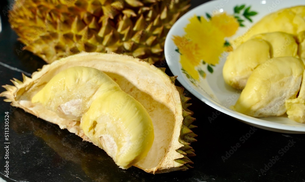 Fresh durian in packaging on white dish with durian peel on banner black background. Durian king of fruit. Tropical fruit. Topview of ripe durian, wood cutting and rind on table Fresh durian in packaging on white dish with durian peel on banner black background. Durian king of fruit. Tropical fruit. Topview of ripe durian, wood cutting and rind on table