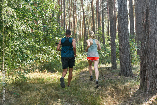 Back view of sports couple running in green forest