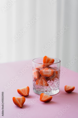 transparent glass of tonic water with cut strawberries on grey background.