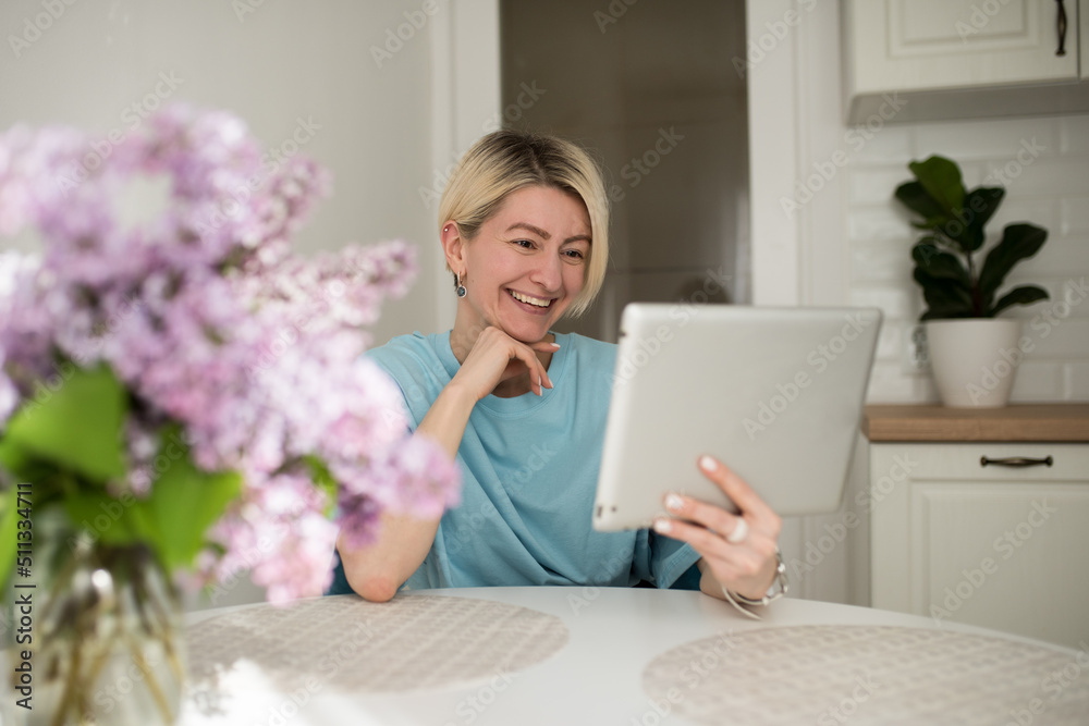 Happy woman with blond hair using digital tablet to make video calls to parents and friends, smiling girl sitting at home in the kitchen cheerfully greets online using a computer webcam, Happy woman with blond hair using digital tablet to make video calls to parents and friends, smiling girl sitting at home in the kitchen cheerfully greets online using a computer webcam,