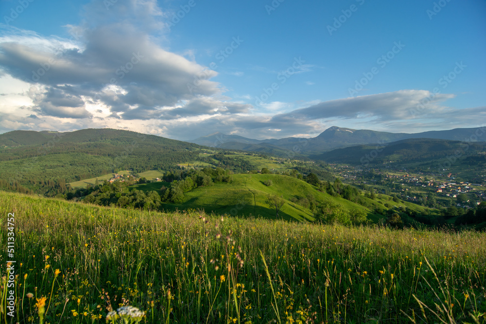 Travel photo of Ukrainian Carpathians. Scenic views of the mountain ranges during sunset, the sky with clouds and the settlements of local residents.