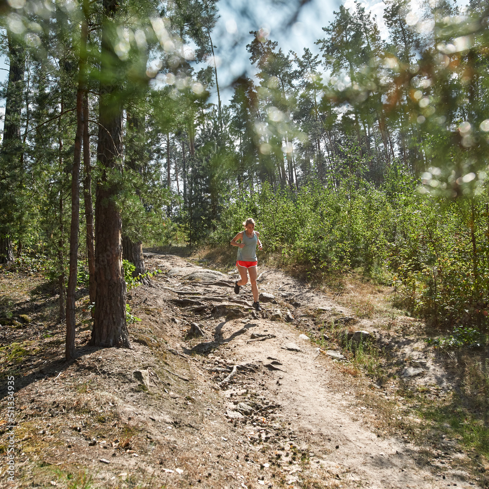 Young sportswoman running on dirt road in forest
