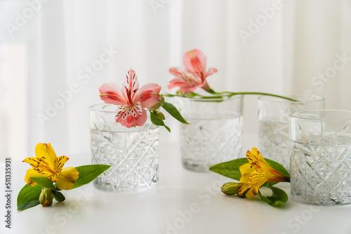 yellow and pink alstroemeria flowers near glasses with water on white tabletop. photo