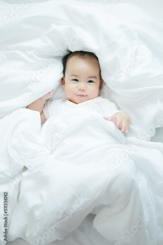 Cute little asian baby on bed with soft blanket indoors