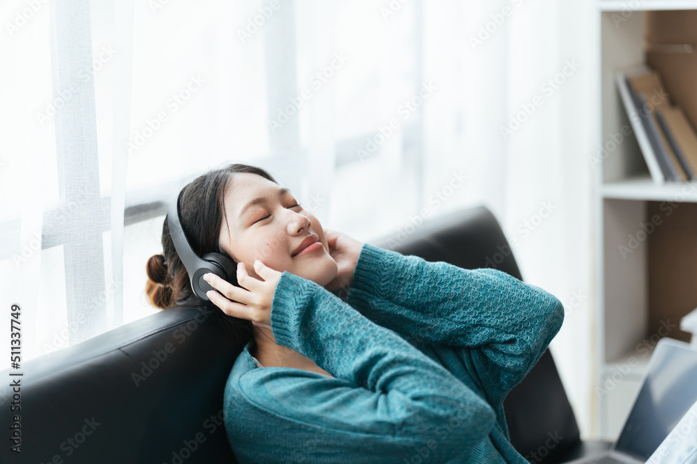 Beautiful asian woman in black headphones sits on sofa and enjoys listening to music, podcast. Beautiful asian woman in black headphones sits on sofa and enjoys listening to music, podcast.