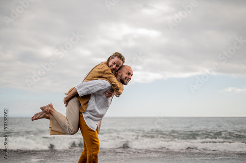 Playful young loving couple on a beach, man holding a girl in the air on his back