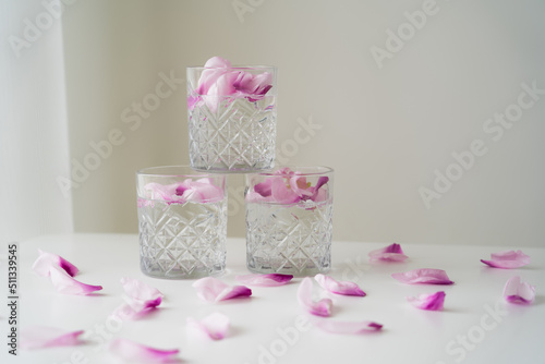 Fototapeta Naklejka Na Ścianę i Meble -  crystal glasses with tonic and floral petals on white surface and grey background.