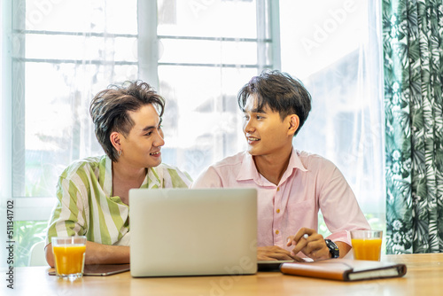 Asian businessman gay work with smile and laugh in office. Attractive male lgbtq collegues working together with using laptop pc and paper showing graphic chart in living room, Lgbt love concept