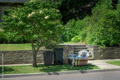 A very colorful and worn chair or love seat is put out onto the curb to be removed by the trashmen this Spring Morning.  Trashcans and chair awaiting picup. photo