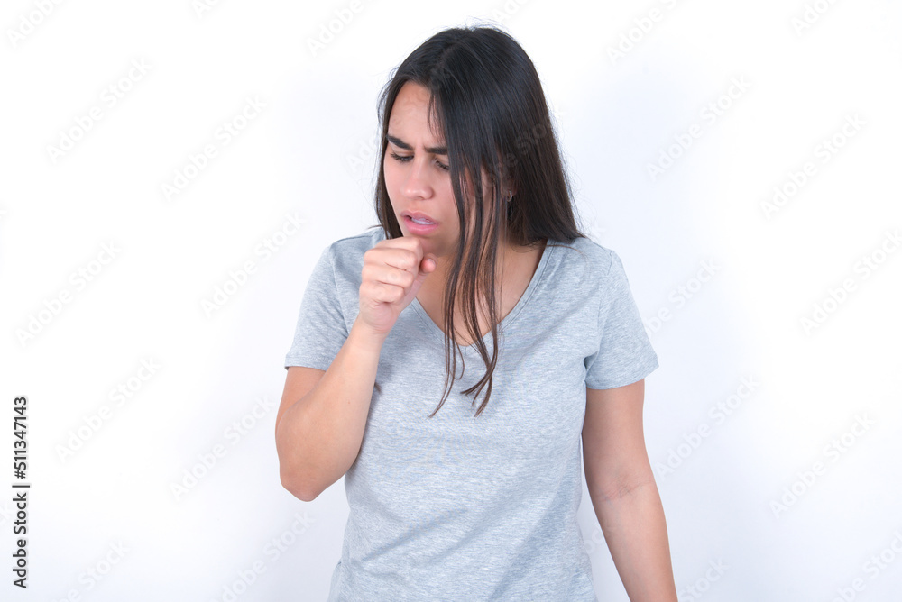 young beautiful brunette woman wearing grey t-shirt over white wall feeling unwell and coughing as symptom for cold or bronchitis. Healthcare concept. young beautiful brunette woman wearing grey t-shirt over white wall feeling unwell and coughing as symptom for cold or bronchitis. Healthcare concept.