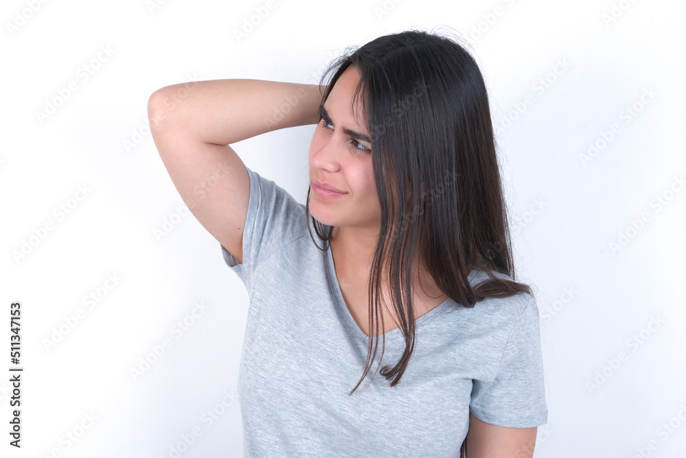 young beautiful brunette woman wearing grey t-shirt over white wall confuse and wonder about question. Uncertain with doubt, thinking with hand on head. Pensive concept. young beautiful brunette woman wearing grey t-shirt over white wall confuse and wonder about question. Uncertain with doubt, thinking with hand on head. Pensive concept.