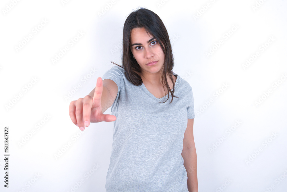 young beautiful brunette woman wearing grey t-shirt over white wall making fun of people with fingers on forehead doing loser gesture mocking and insulting. young beautiful brunette woman wearing grey t-shirt over white wall making fun of people with fingers on forehead doing loser gesture mocking and insulting.