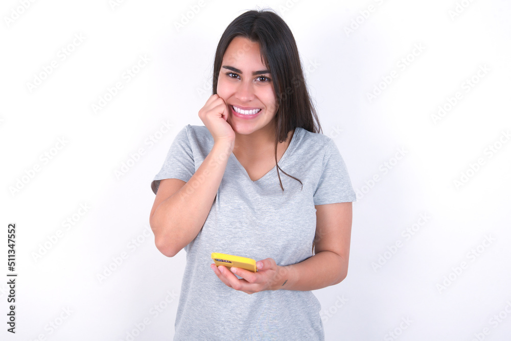 Joyous Young beautiful brunette woman wearing gray poses with mobile phone device, types text message on modern smartphone, watches funny video during free time, enjoys good internet connection, Joyous Young beautiful brunette woman wearing gray poses with mobile phone device, types text message on modern smartphone, watches funny video during free time, enjoys good internet connection,