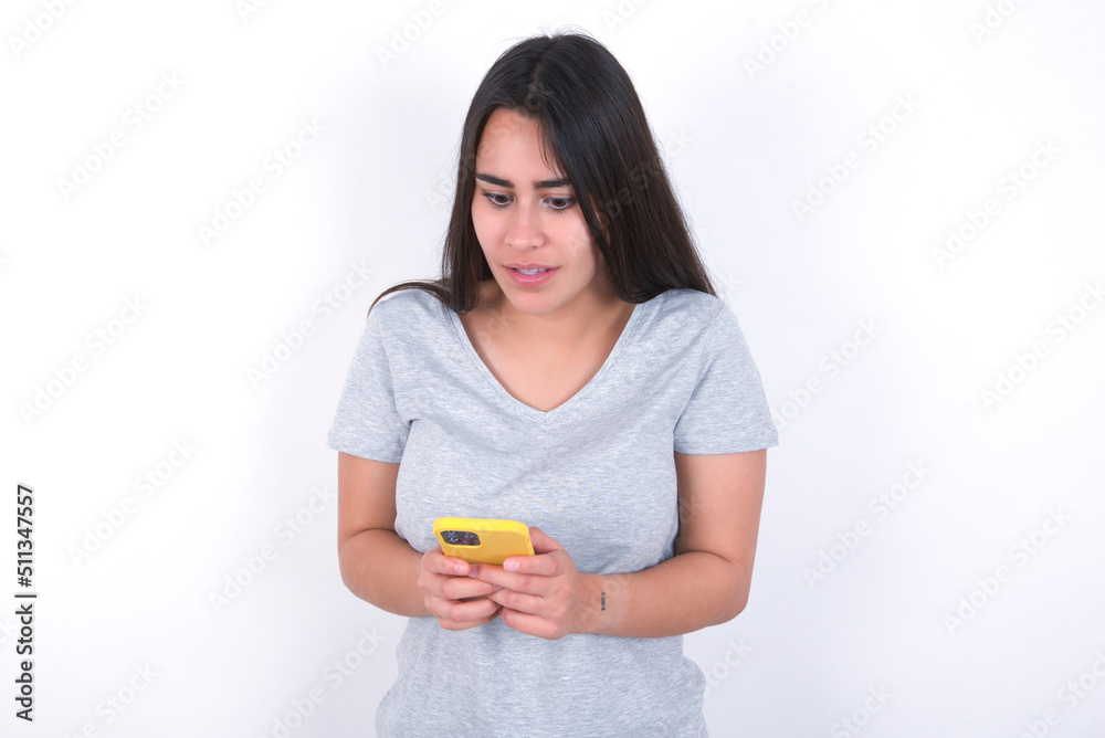 Young beautiful brunette woman wearing gray T-shirt over white wall using mobile phone chatting free time .