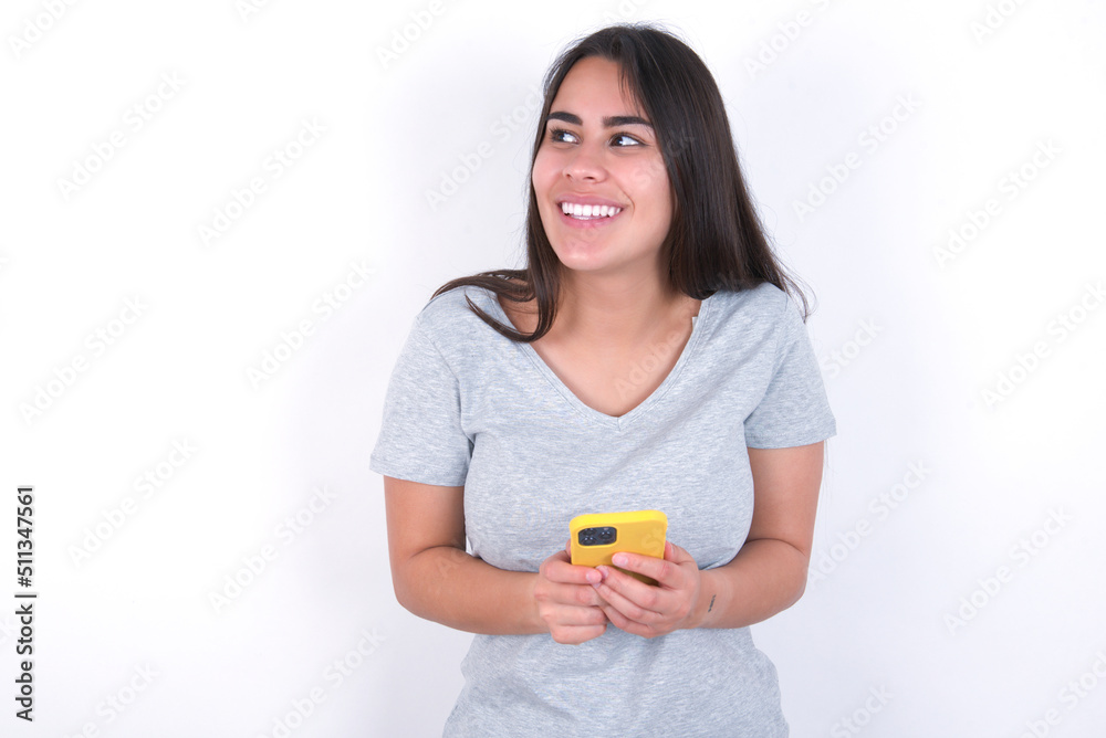 Young beautiful brunette woman wearing gray T-shirt over white wall holding in hands showing new cell Young beautiful brunette woman wearing gray T-shirt over white wall holding in hands showing new cell