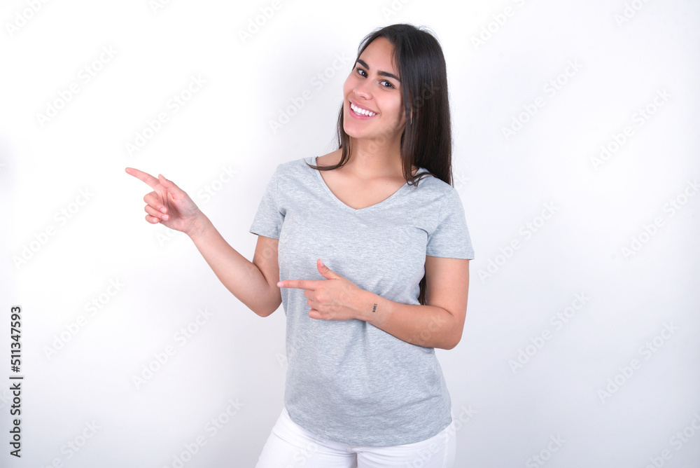 Young beautiful brunette woman wearing gray T-shirt over white wall point at copyspace recommend sales discounts Young beautiful brunette woman wearing gray T-shirt over white wall point at copyspace recommend sales discounts