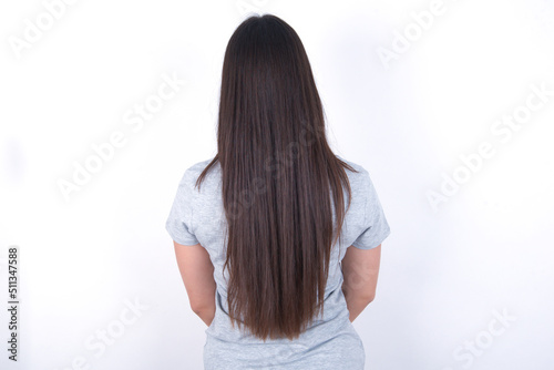 The back view of a Young beautiful brunette woman wearing gray T-shirt over white wall. Studio Shoot.