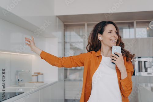 Happy spanish girl in airpods is singing with mobile telephone as with microphone. photo