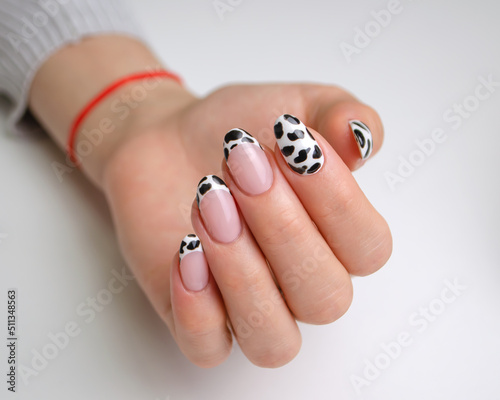 The hands of a young woman with a manicure. Nails are covered with gel polish with a French jacket and a black and white pattern