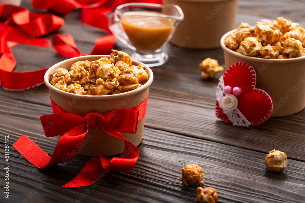 Carton buckets with caramelized popcorn and valentine decorations on kitchen table food background