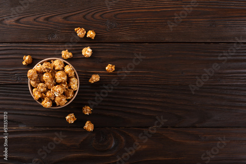 Caramelized popcorn in paper bucket on wooden kitchen table flat lay