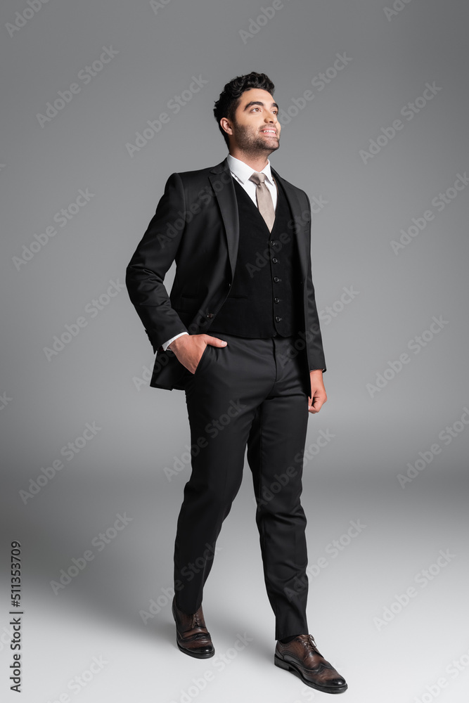 full length of stylish muslim groom in suit posing with hand in pocket while standing on grey. full length of stylish muslim groom in suit posing with hand in pocket while standing on grey.