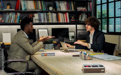 Two diverse Caucasian and African businessman seriously discussing with argument, disputing while sitting in modern meeting room at office. They disatisfied, disagreed about the project idea.