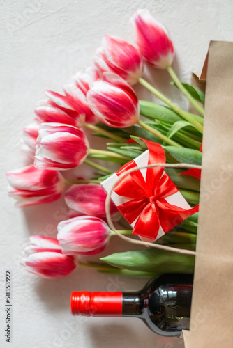Fototapeta Naklejka Na Ścianę i Meble -  Mother's Day or Women's Day, birthday, wedding congratulation. Spring tulips with a gift box and a bottle of wine in a paper bag.