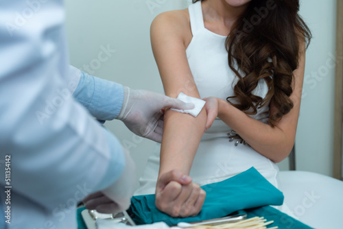 Hand of Caucasian male doctor in white medical gloves using a piece of cotton pad press on the injection site on Asian female patient's arm that place on table with green cloth and injection device.