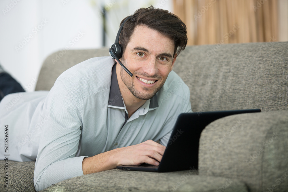 man layed on sofa wearing headset and using laptop man layed on sofa wearing headset and using laptop