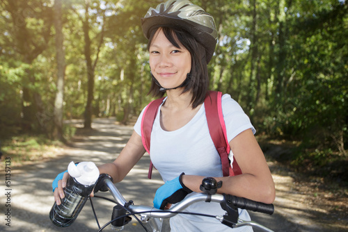 young asian woman smiling cheerfully while stood beside her bicycle