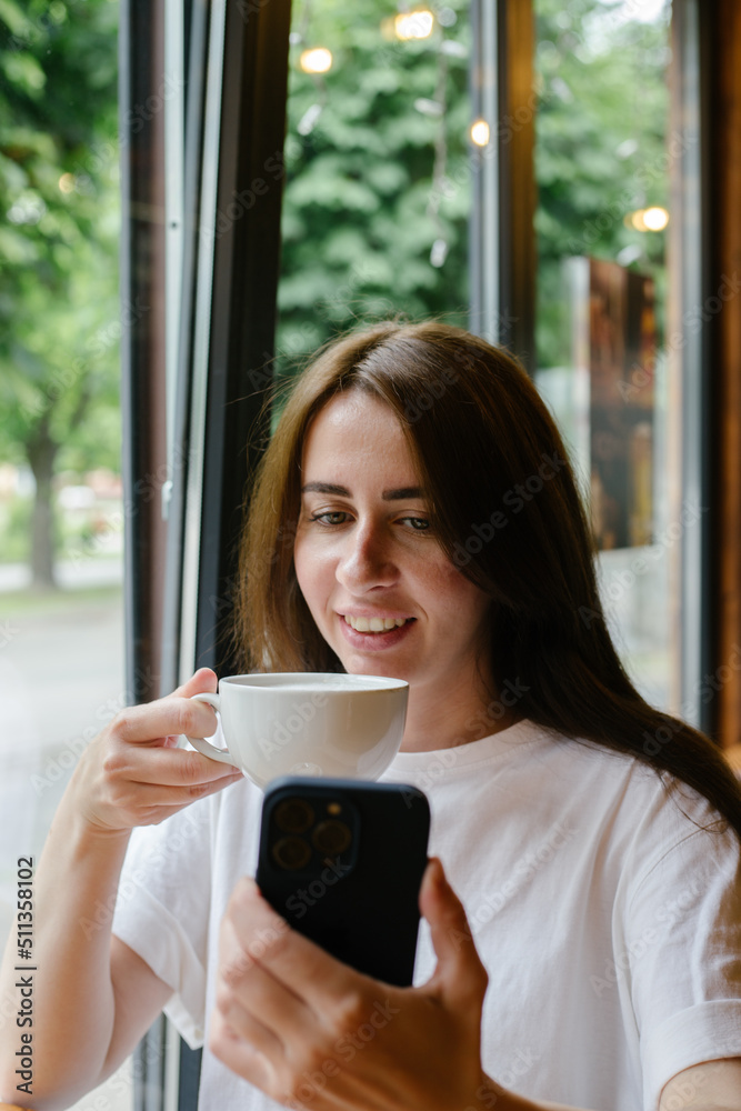 woman drinking coffee in cafe and using her smartphone woman drinking coffee in cafe and using her smartphone