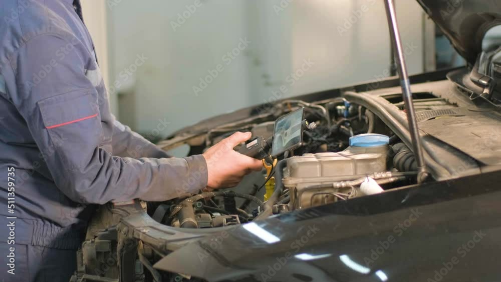 Hands of car mechanic check the vehicle engine with technical endoscope with rotary camera and mobile phone. Repair of engine head and valves.