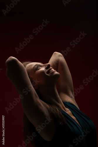 Cute girl against dark red background. Brunette lady wearing fancy shirt with hands up looking up.